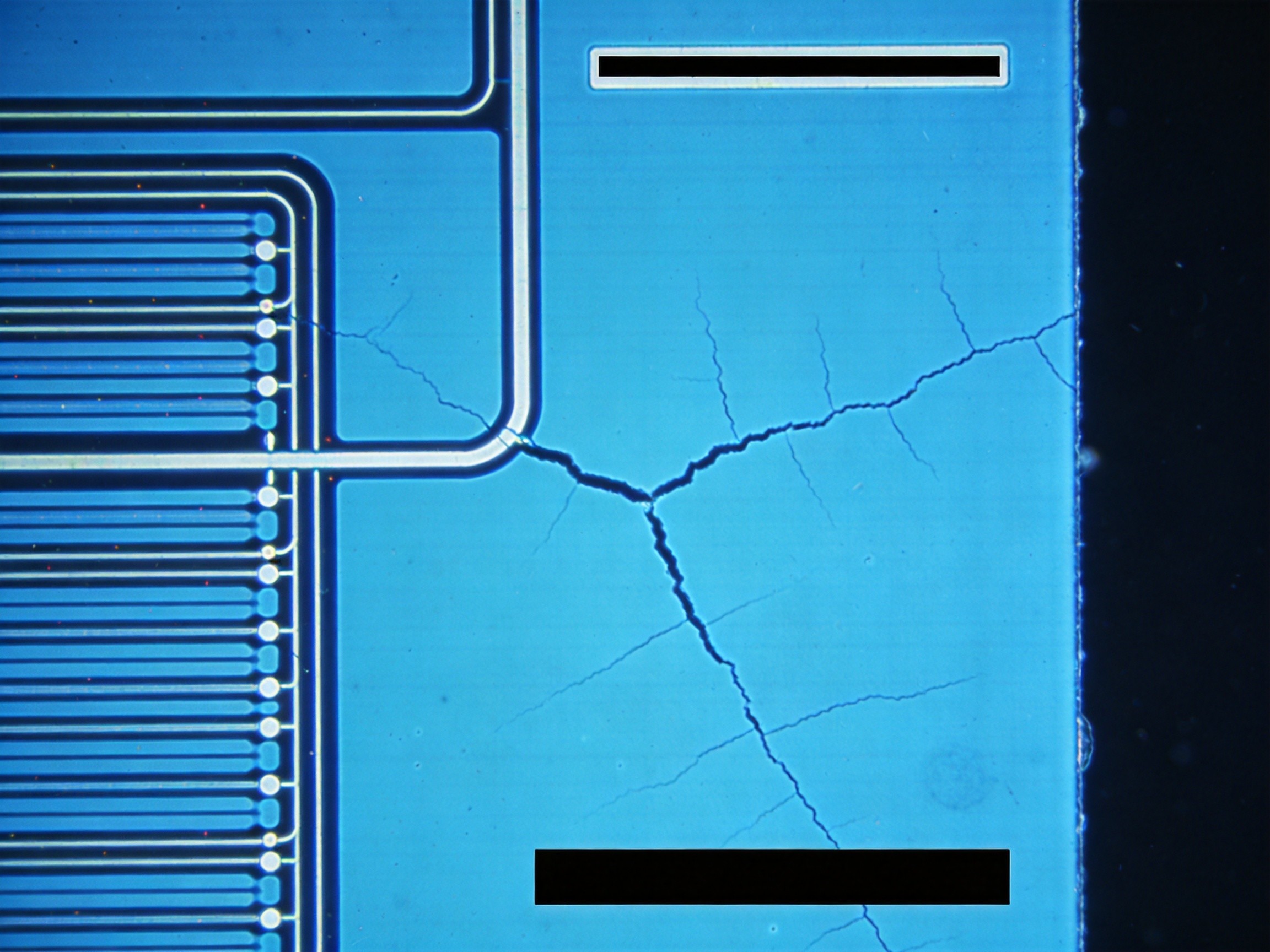 Microscope image of ITO electrode micro-crack propagation on touch sensor glass, showing fracture pattern from thermal cycling stress