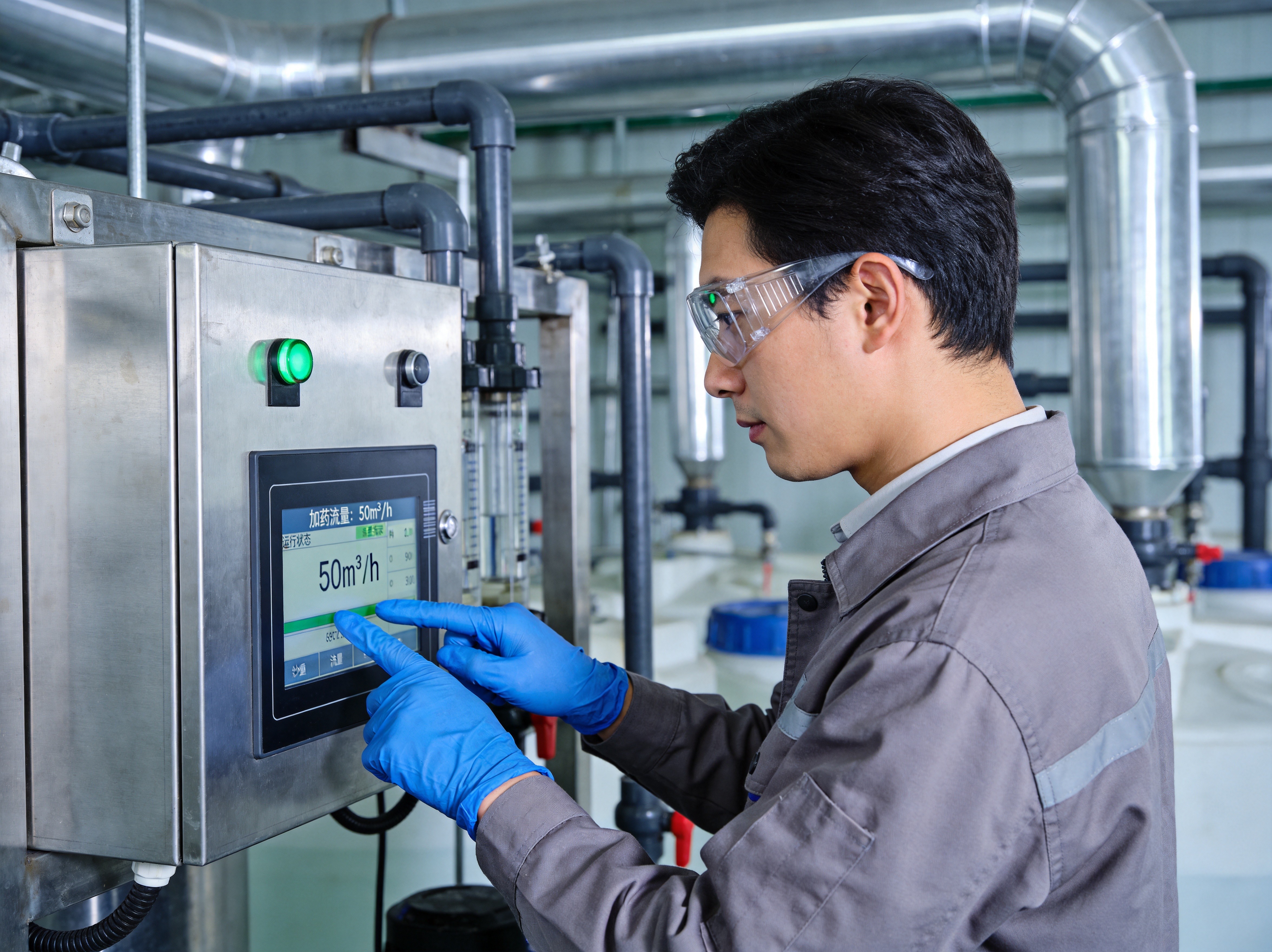 A water treatment plant operator in protective equipment using a gloved hand to interact with a panel PC touchscreen displaying chemical dosing flow rates and SCADA system status indicators