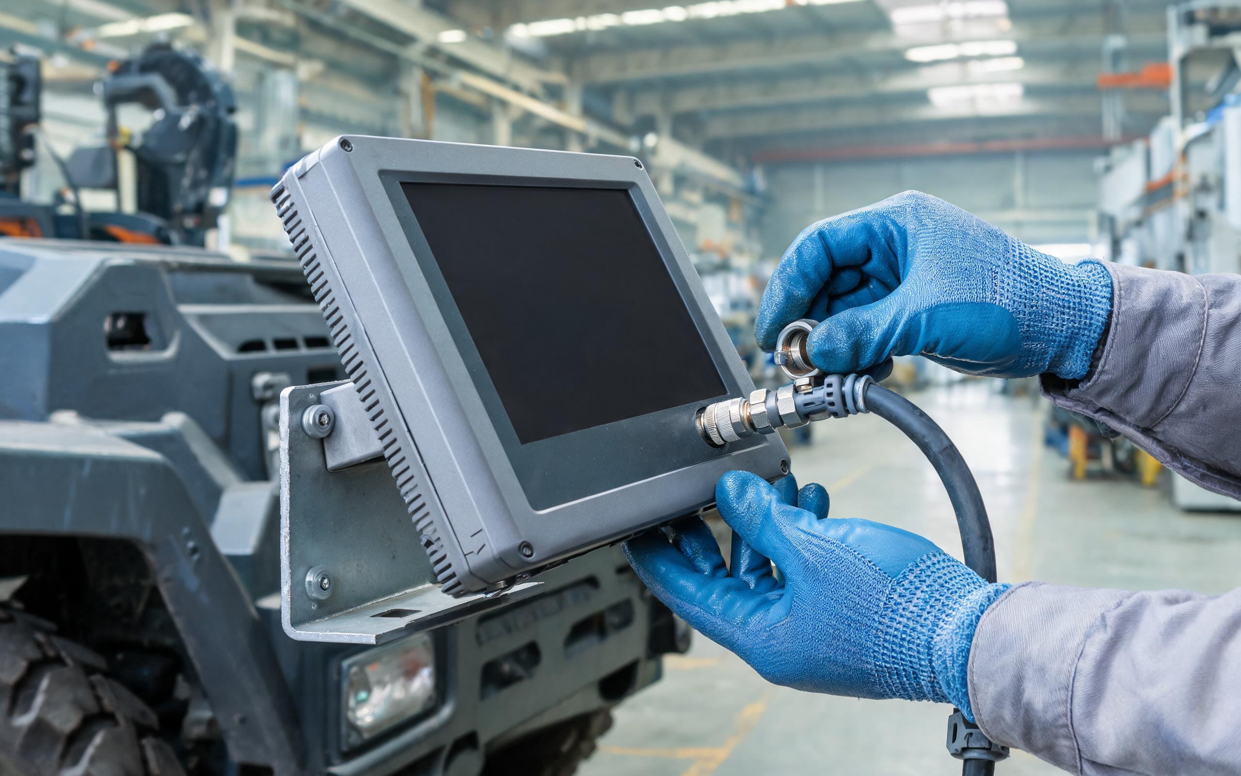 Screw-lock M12 cable mating on a vehicle-mounted panel PC gloved technician tightening a screw-lock M12 connector cable onto a fanless industrial panel pc on a factory vehicle