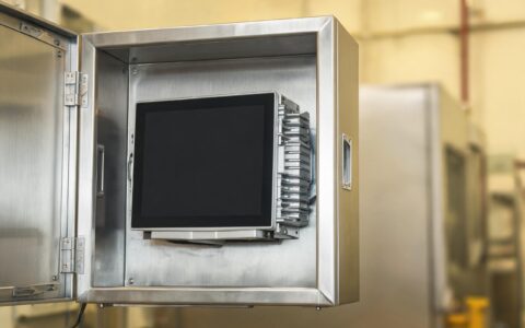 fanless panel pc mounted inside a sealed stainless steel wall cabinet with the rear aluminum housing and stacked thermal interface layers exposed, industrial engineering photography, dark display screen no text