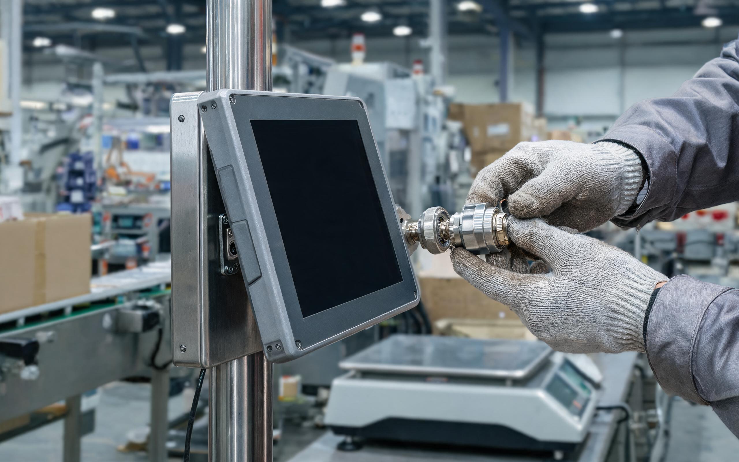 Live connector re-seating on an isolated panel technician commissioning a rugged touch screen pc at a logistics filling line workstation, plugging a sealed serial connector while the line runs, realistic industrial photography, dark screen no text